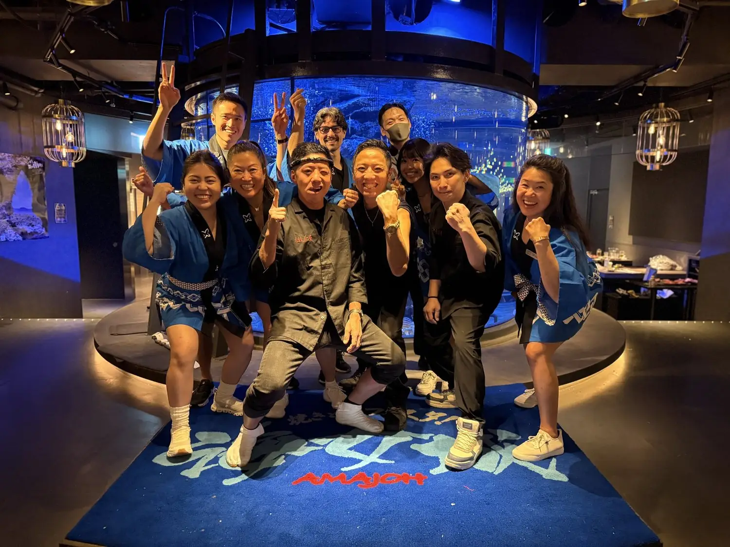 The team in matching blue kimonos and headbands, fists up, in front of the giant fish tank at the sushi spot