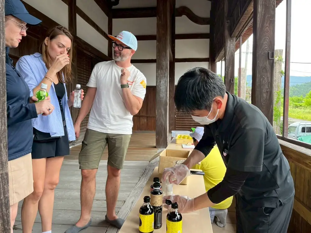 Guests tasting from little cups as a host pours from dark glass bottles