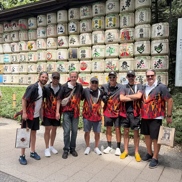 A team in matching flame shirts in front of a wall of sake barrels